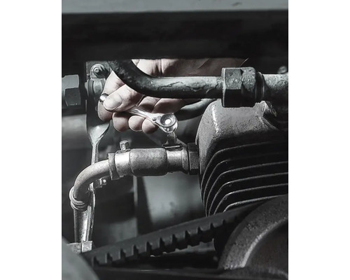 Hand draait bout aan op motor met ratelsleutel