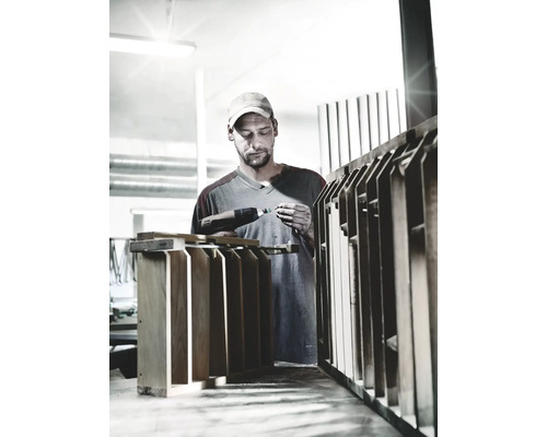 Ambachtsman werkt met een accuboormachine aan een houten object in een werkplaats.