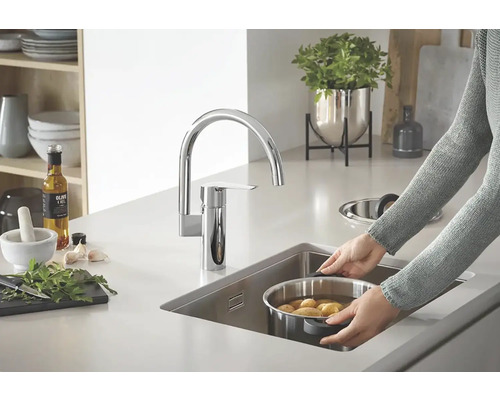 Keukenscène met spoelbakmengkraan, gootsteen en persoon die een pan met aardappelen vasthoudt.