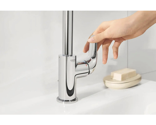 Glanzende wastafelkraan met eenhendelmengkraan en Grohe logo wordt bediend door een hand.