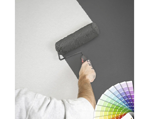 Iemand schildert een muur met een verfroller en een kleurenwaaier.