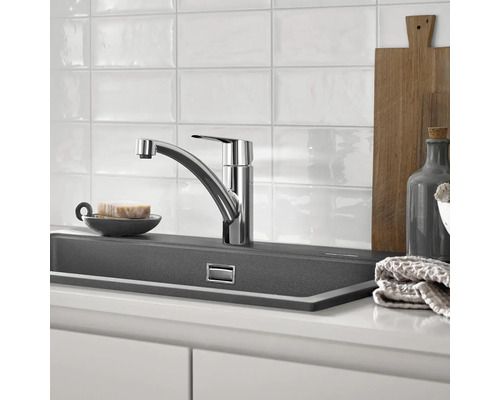 Keukenscène met gootsteenkraan, spoelbak en keukengerei.