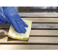 Een hand met beschermende handschoen reinigt een houten oppervlak met een doek.