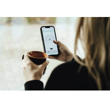 Vrouw met kop en smartphone voor temperatuurregeling