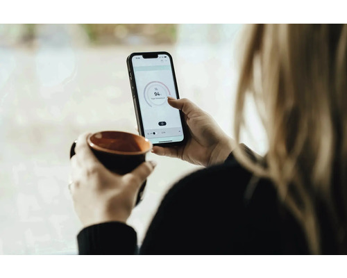 Vrouw met kop en smartphone voor temperatuurregeling