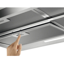 Detailopname van een afzuigkap met metalen filter en een vinger op de schakelaar