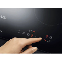 AEG kookplaat met aanraakbedieningspaneel en een hand die de temperatuur instelt