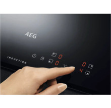 Close-up van een AEG inductiekookplaat met een hand die het vermogensniveau aanpast.