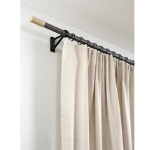 Donkere gordijnroede van hout en metaal met lichte eindkappen, zwarte ringen en beige gordijn aan een zwarte wandsteun.