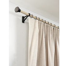 Gordijnroede in houtlook met zwarte metalen steunen en ringen, met een beige gordijn van gestructureerde stof gemonteerd aan de muur.