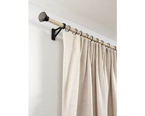 Gordijnroede in houtlook met zwarte metalen steunen en ringen, met een beige gordijn van gestructureerde stof gemonteerd aan de muur.