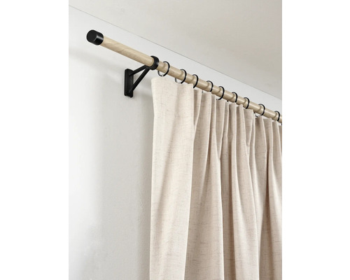 Gordijnroede van licht hout met zwarte metalen steunen en ringen, voorzien van een lichtbeige gordijn met linnenstructuur.