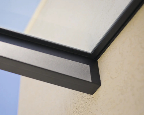 Detail van een donker aluminium frame voor een terrasoverkapping met glaselement aan een buitenmuur.