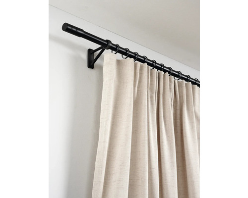 Zwarte metalen gordijnroede met ringen en beige gordijn van gestructureerde stof aan een muur gemonteerd.