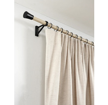 Houten gordijnroede met zwarte eindknoppen en ringen en een beige gordijn met structuur aan de wand.
