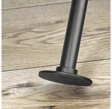 Detailopname van een zwarte meubelpoot met voet op een houten vloer.