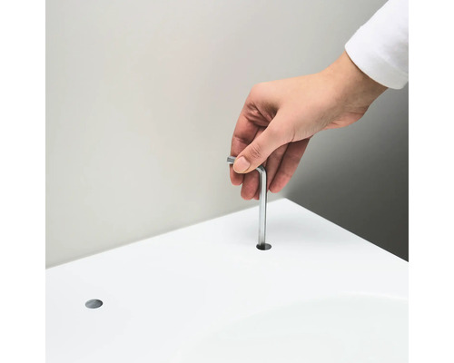 Een persoon steekt een inbussleutel in een gat in een wit oppervlak