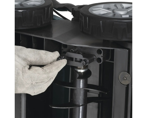 Hand in werkhandschoen bij de montage of instelling van een tuinmachine met wielen en messen.
