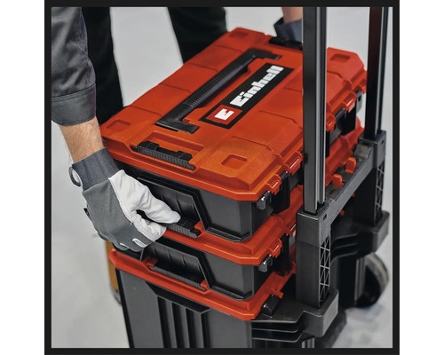 Einhell E-Case systeem gereedschapskoffers gestapeld op een trolley, vastgehouden door een hand met werkhandschoen.