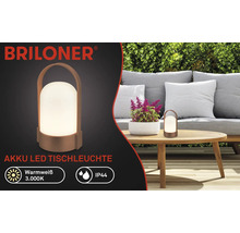 Briloner Logo, oplaadbare LED-tafellamp op houten tafel in tuin met bank en heg, warm wit licht 3000 Kelvin, spatwaterdicht IP44.