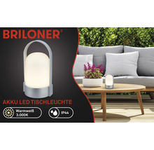 Briloner Logo, accu-led-tafellamp, warmwit 3000 kelvin, IP44 spatwaterdicht, draagbaar met handgreep, in de tuin op een houten tafel.