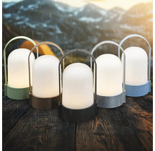 Vijf draagbare outdoor LED-lantaarns in verschillende kleuren op een houten tafel in de regen met bergen op de achtergrond.