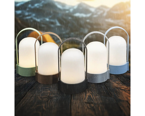 Vijf draagbare outdoor LED-lantaarns in verschillende kleuren op een houten tafel in de regen met bergen op de achtergrond.