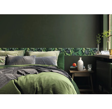 Slaapkamer met donkergroene muur en een behangrand met bladmotief. Een bed met groen beddengoed staat naast een houten nachtkastje.