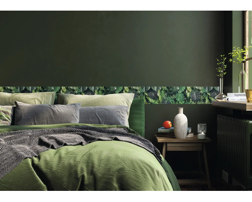 Slaapkamer met donkergroene muur en een behangrand met bladmotief. Een bed met groen beddengoed staat naast een houten nachtkastje.