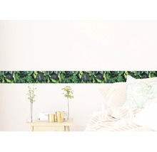 Zelfklevende behangrand met tropisch monstera bladerpatroon in een lichte slaapkamer boven een bed.
