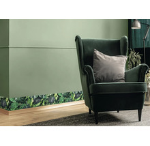 Behangrand met botanisch bladerenpatroon op een wand in een woonkamer met fauteuil en houten vloer.