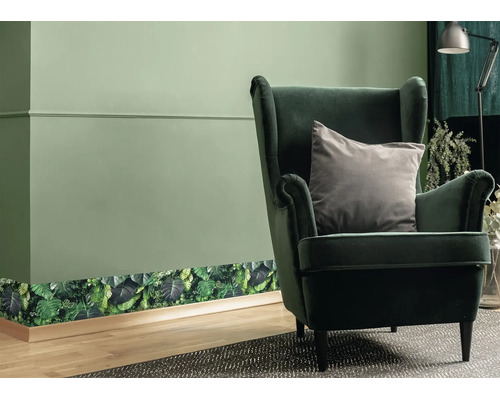 Behangrand met botanisch bladerenpatroon op een wand in een woonkamer met fauteuil en houten vloer.