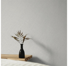 Vliesbehang met fijne linnenstructuur op een wand achter een vaas met een gedroogd blad op een houten tafel.