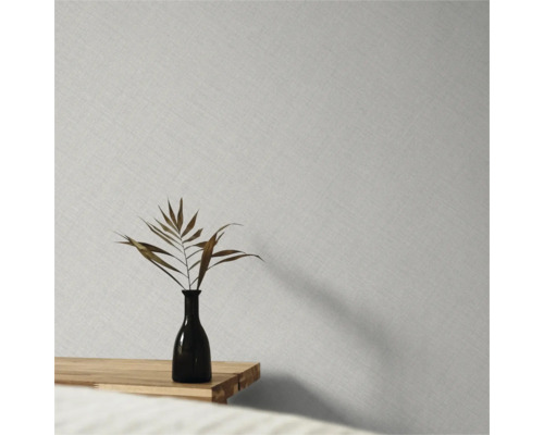 Vliesbehang met fijne linnenstructuur op een wand achter een vaas met een gedroogd blad op een houten tafel.