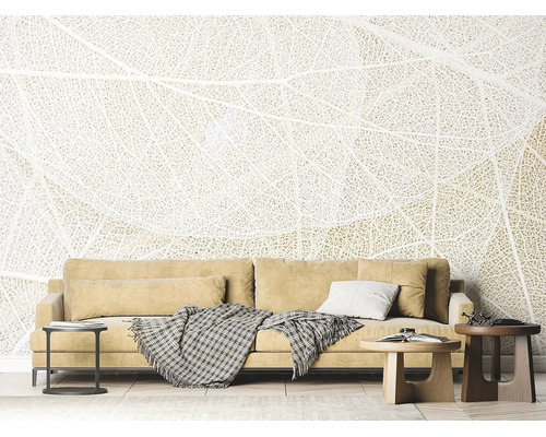 Fotobehang met verfijnd bladstructuurmotief in een lichte woonkamer achter een bank met kussens en bijzettafels.