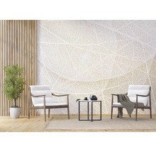Lichte woonkamer met fotobehang in bladnerf-design, twee houten fauteuils met witte kussens, zwarte bijzetmeter en kamerplant.
