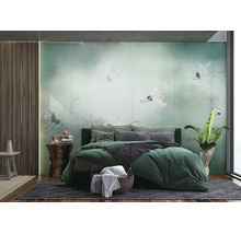Fotobehang in slaapkamer met witte kraanvogels in mistig bos, groen bed met kussens, houten panelen aan wand en kamerplant.