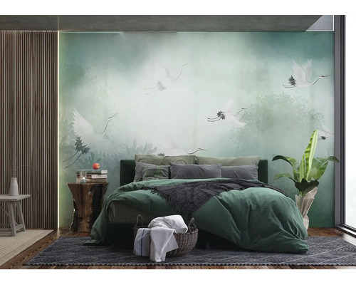 Fotobehang in slaapkamer met witte kraanvogels in mistig bos, groen bed met kussens, houten panelen aan wand en kamerplant.