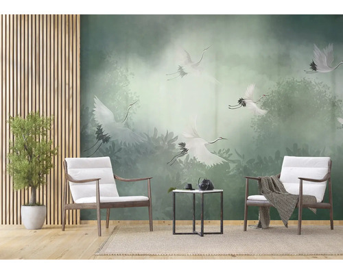 Fotobehang met witte kraanvogels boven een groen nevelwoud in een modern ingerichte woonkamer met houten fauteuils en bijzettafel.