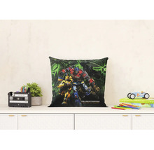 Vierkant sierkussen met Transformers Rise of the Beasts print op een dressoir. De lichte kamer bevat een plant en speelgoed.