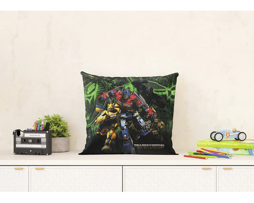 Vierkant sierkussen met Transformers Rise of the Beasts print op een dressoir. De lichte kamer bevat een plant en speelgoed.