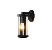 Moderne buitenwandlamp in cilindervorm van zwart metaal en helder glas met ingeschakelde lichtbron.