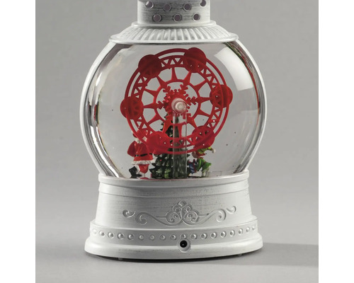 Decoratieve sneeuwbollantaarn met een rood reuzenrad, kerstboom en kerstmanfiguur op een witte, bewerkte voet.