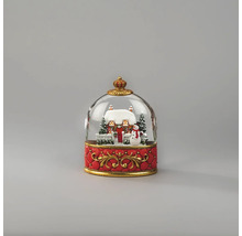 Sneeuwbol met besneeuwd huis, sneeuwman en dennenbomen op een rode voet met gouden ornamenten.