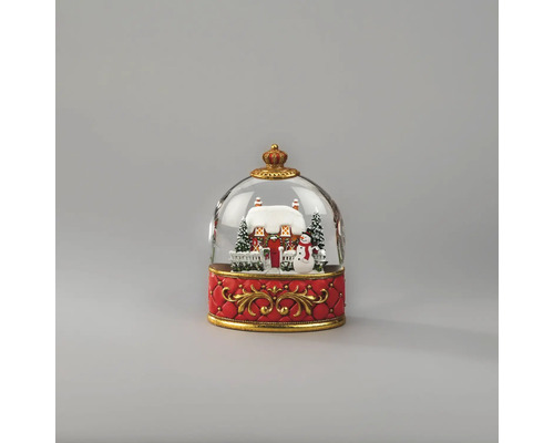 Sneeuwbol met besneeuwd huis, sneeuwman en dennenbomen op een rode voet met gouden ornamenten.