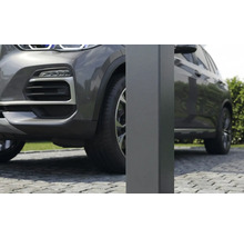 Dichtbij opname van een vierkante metalen paal voor een carport op een oprit van kasseien naast een grijze auto.