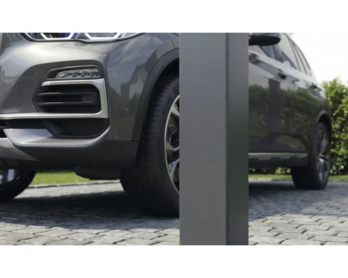 Dichtbij opname van een vierkante metalen paal voor een carport op een oprit van kasseien naast een grijze auto.