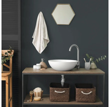 Moderne badkamer met een witte opzetwastafel op een houten wastafelmeubel, een hoge zilveren kraan en een zeshoekige spiegel voor een donkere muur.
