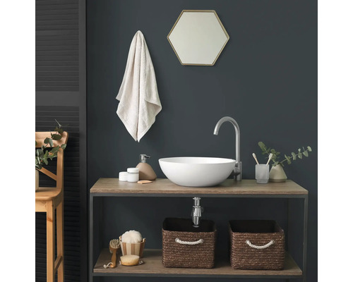 Moderne badkamer met een witte opzetwastafel op een houten wastafelmeubel, een hoge zilveren kraan en een zeshoekige spiegel voor een donkere muur.