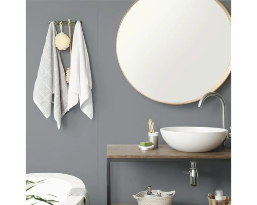 Moderne badkamer met ronde spiegel, witte opzetwastafel op een houten blad, grijze wand en wandhaak met handdoeken.